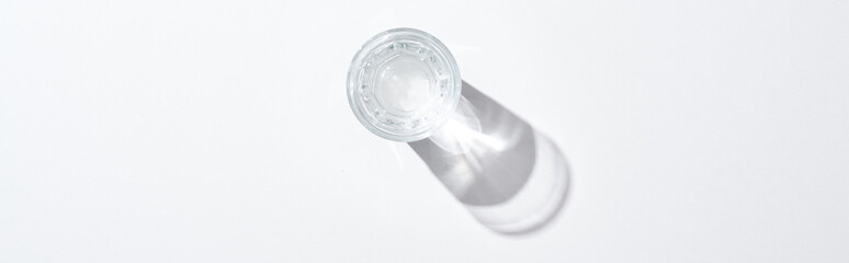 top view of transparent glass with water on white surface with shadow, panoramic shot