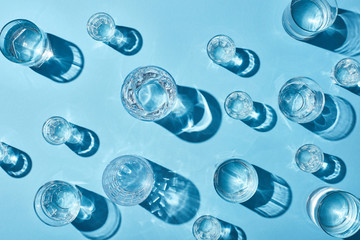 Wall Mural - top view of transparent glasses with clear water and shadows on blue background