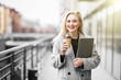 © dianagrytsku - Joyful european woman walking outdoor with silver laptop and takeaway coffee in hands
