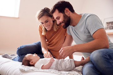 Wall Mural - Loving Parents With Newborn Baby Lying On Bed At Home In Loft Apartment