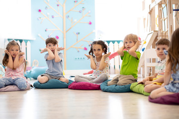 Wall Mural - Kids seating on floor and show gestures making task in daycare