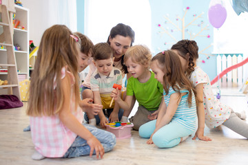 Preschool teacher plays with group of kids sitting on a floor at kindergarten