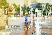 A Boy Playing With Water In Park Fountain. Hot Summer. Happy Young Boy Has Fun Playing In Water Fountains