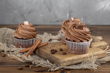 brown cupcakes with cocoa cream, cinnamon and coffee on wooden background