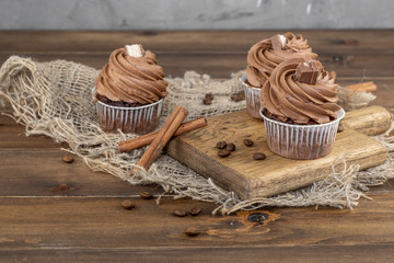 brown cupcakes with cocoa cream, cinnamon and coffee on wooden background