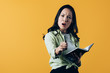 © LIGHTFIELD STUDIOS - angry asian woman with notebook and pen, isolated on yellow