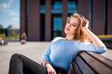 Fototapeta Przestrzenne - Young woman sitting on bench in city urban space during summer