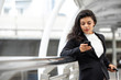 © Atstock Productions - Young Latin businesswoman using cell phone and holding handle of trolley bag