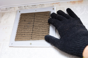 repair service man removing a dirty air filter on a house so he can replace it with a new clean. Extremely dirty and dusty white plastic ventilation air grille at home close up, harmful for health 