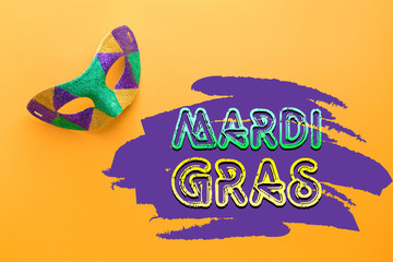 Festive mask with text MARDI GRAS (also known as Fat Tuesday) on color background