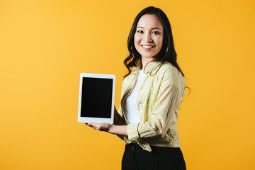 Wall Mural - smiling asian woman showing digital tablet with blank screen, isolated on yellow