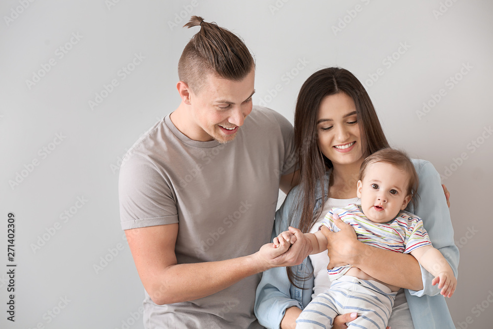 Happy parents with cute little baby on light background