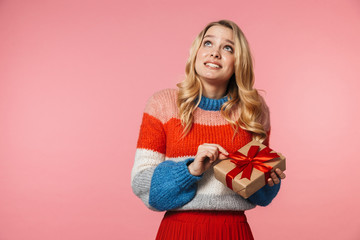 Young pretty beautiful woman posing isolated over pink wall background holding present gift box.