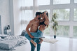Pure feelings. Handsome young shirtless man carrying semi-dressed attractive woman while standing in the bedroom
