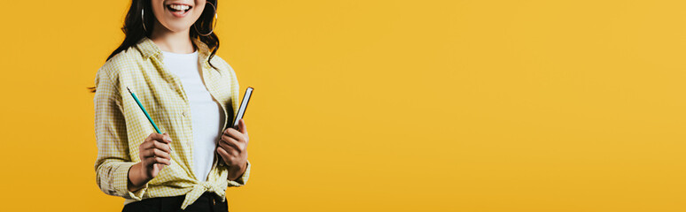 Wall Mural - cropped view of girl with notebook and pen, isolated on yellow