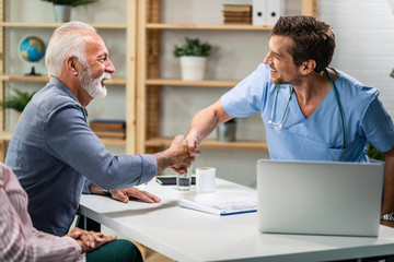 Wall Mural - Happy senior man and doctor shaking hands while meeting at doctor's office.