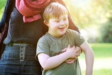 Little Boy With Down Syndrome Cuddling Up To His Mother In A Park