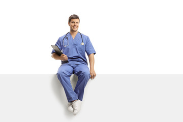 Wall Mural - Young male doctor in a blue uniform sitting on a white panel