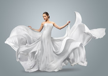 Fashion Portrait Of A Beautiful Woman In A Waving White Dress. Light Fabric Flies In The Wind.