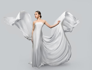 Fashion portrait of a beautiful woman in a waving white dress. Light fabric flies in the wind.