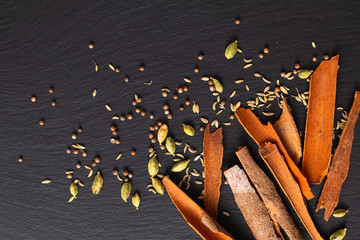 Wall Mural - Food concept assortment Oriental spices cardamom pods, coriander seeds, fennel and Cinnamon Cassia Bark Sticks on black slate stone with copy space