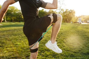 Wall Mural - Handsome young strong sports man posing outdoors at the nature park location make exercises with fitness equipment.