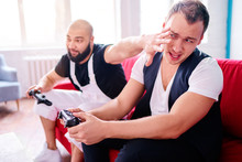 Friends And Video Games. Two Handsome Young Men Playing Video Games While Sitting On Sofa