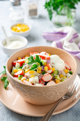 Wall Mural - Salad with crab sticks, sweet corn, cucumbers, boiled eggs, onion and rice in bowl on concrete background. Russian cuisine. Selective focus.