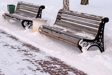 two benches in the Park in the winter around the snow and a path of brick