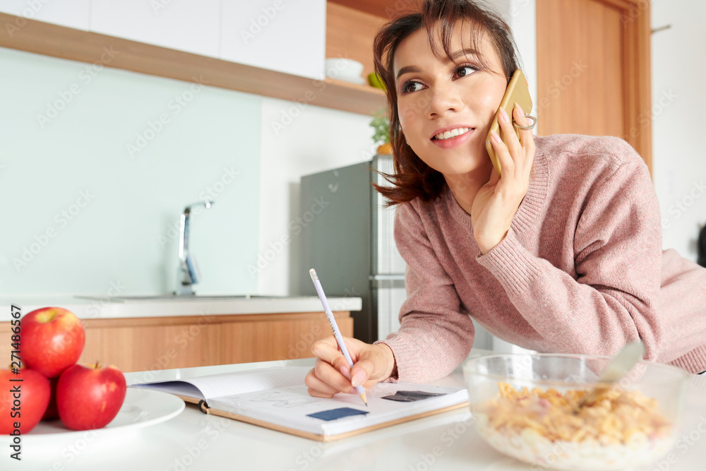 Photo Stock Young smiling woman making notes in notepad at the table ...