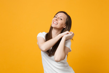 Wall Mural - Portrait of smiling joyful young woman in white casual clothes clenching fists, looking camera isolated on bright yellow orange wall background in studio. People lifestyle concept. Mock up copy space.