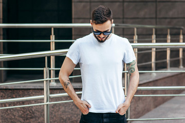 Poster - A young stylish man with a beard in a white T-shirt and glasses. Street photo