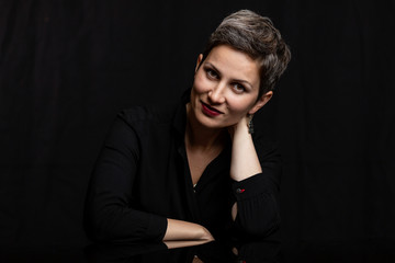 Smiling middle-aged woman with a short haircut, close-up. Portrait on a black background.