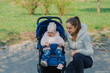 © combo1982 - Young mother with a baby in a stroller in a summer park.
