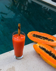 Fresh orange papaya juice in glass with bamboo tube on a  stone background near waterpool. Tropical Fruit. Top view. Free text space.