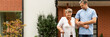 Panoramic view of happy senior lady with walking stick going for at walk with handsome male nurse in the garden of nursing home