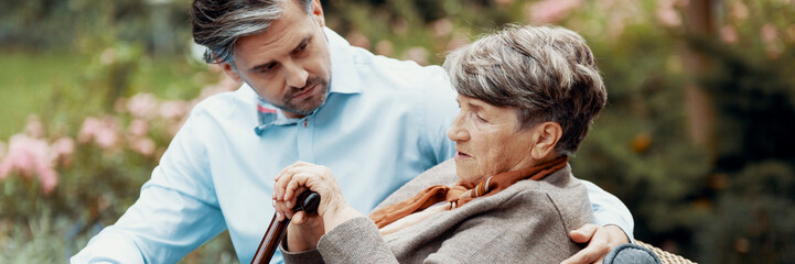 Poster - Panoramic view of worried handsome son with his sick old mother sitting in the park