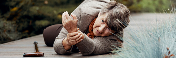 Poster - Elderly lady lies on the ground and takes her pulse