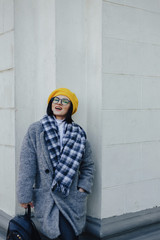 Wall Mural - Attractive young girl in glasses in coat and yellow Beret on a simple light background