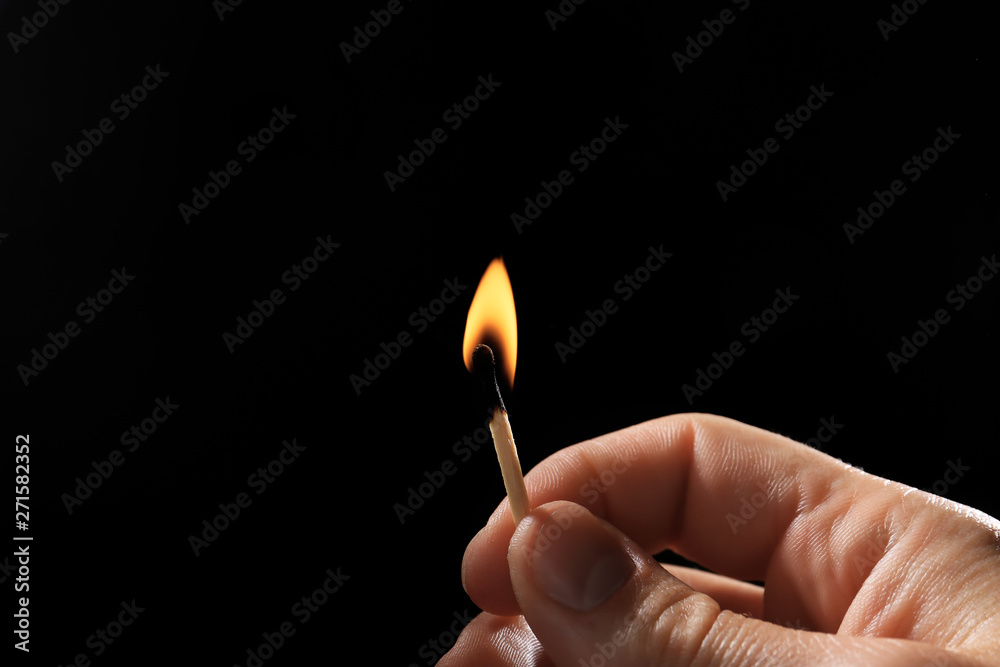 Male hand with burning match on dark background