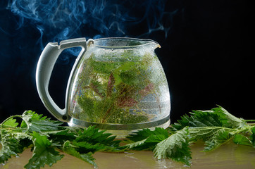 Tea teapot of medicinal nettle with nettle leaves and smoke on a black background