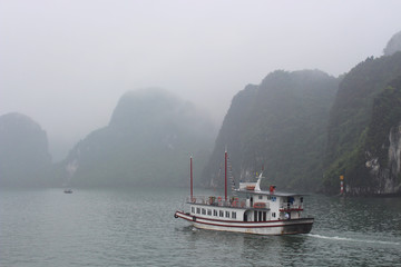 romantic and mysterious misty day in halong bay, vietnam. Boats in ha long bay with misty cliffs on the background