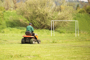 Worker on a large green lawn mower mows the grass on the football field. Landscape design and maintenance of green areas of the sports complex. Making grass stadium before the match. Human labor