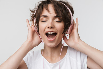 Wall Mural - Pretty excited happy woman posing isolated over white wall background listening music with headphones.