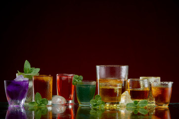  Different alcoholic drinks in clear glasses with ice and mint on red background