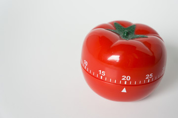 Close up view of mechanical tomato shaped kitchen clock timer for cooking & studying. Used for pomodoro technique for time and productivity management. Isolated on white background, set at 20 minutes.