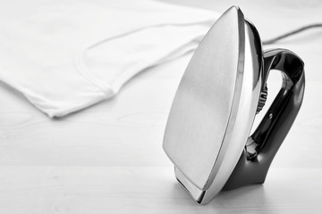 Vintage iron placed vertically on ironing table and a white t-shirt on the background