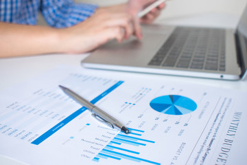 Poster - The hands of businessmen wearing a plaid shirt using mobile phones and laptop computers with financial graphs. Close up.