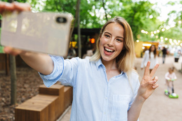 Sticker - Excited happy young woman posing outdoors in park take a selfie by mobile phone.