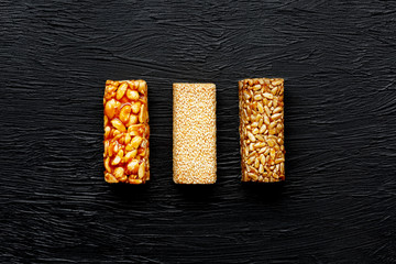 Cereal granola bar with peanuts, sesame and sunflower seeds on a cutting board on a dark stone table. View from above. Three Assorted Bars